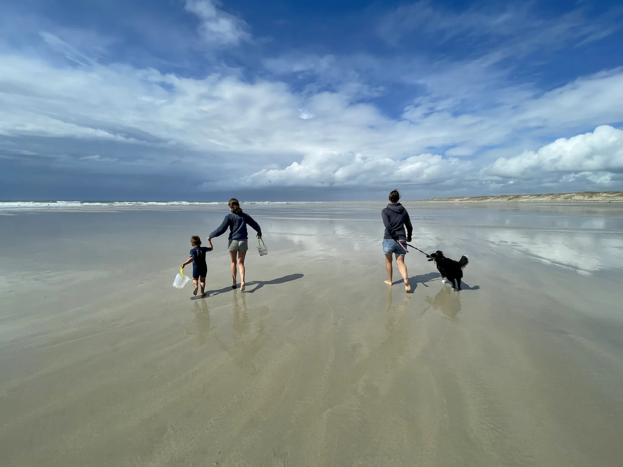 Familie läuft barfuß über einen Sandstrand Richtung Wasser – glutenfreier Urlaub